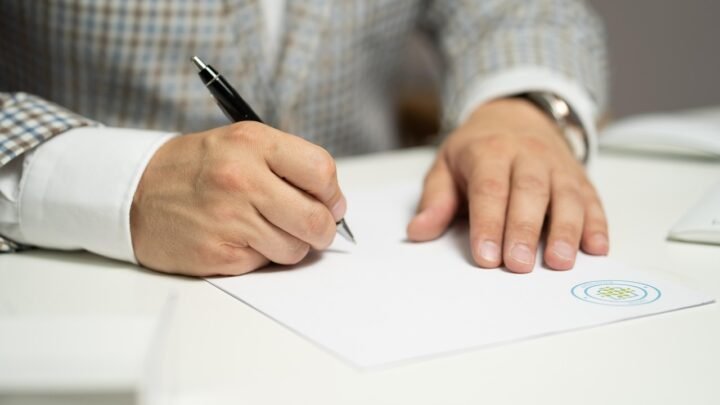 A person signing a contract document, representing the commitment involved in an SEO agency six-month minimum agreement.